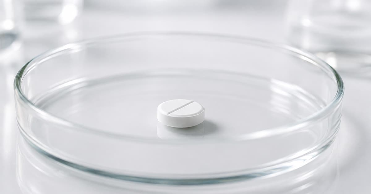 A single white tablet in a glass petri dish on a lab bench