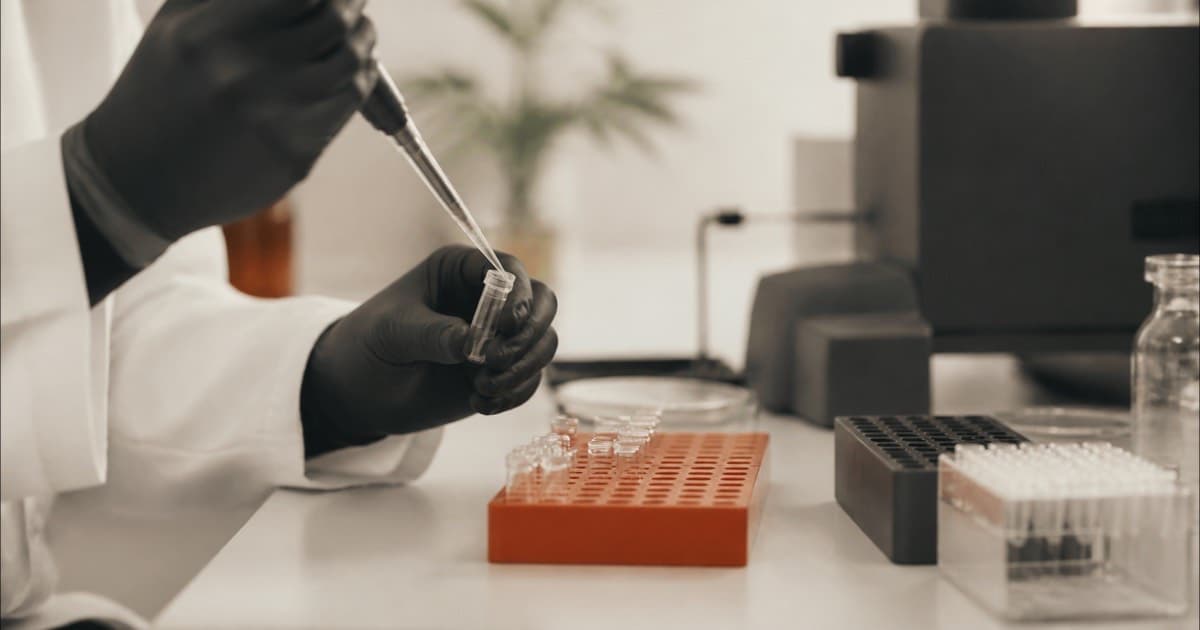 A researcher's gloved hands using a pipette in a laboratory, face not shown
